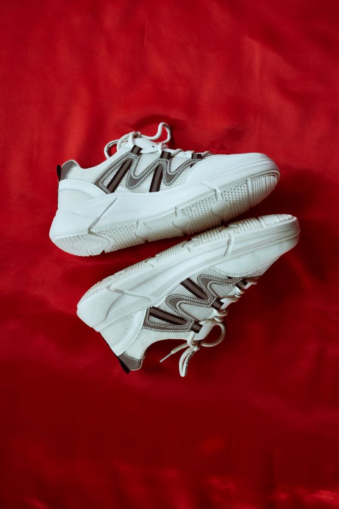 Pair of modern white sneakers placed on a striking red fabric backdrop.