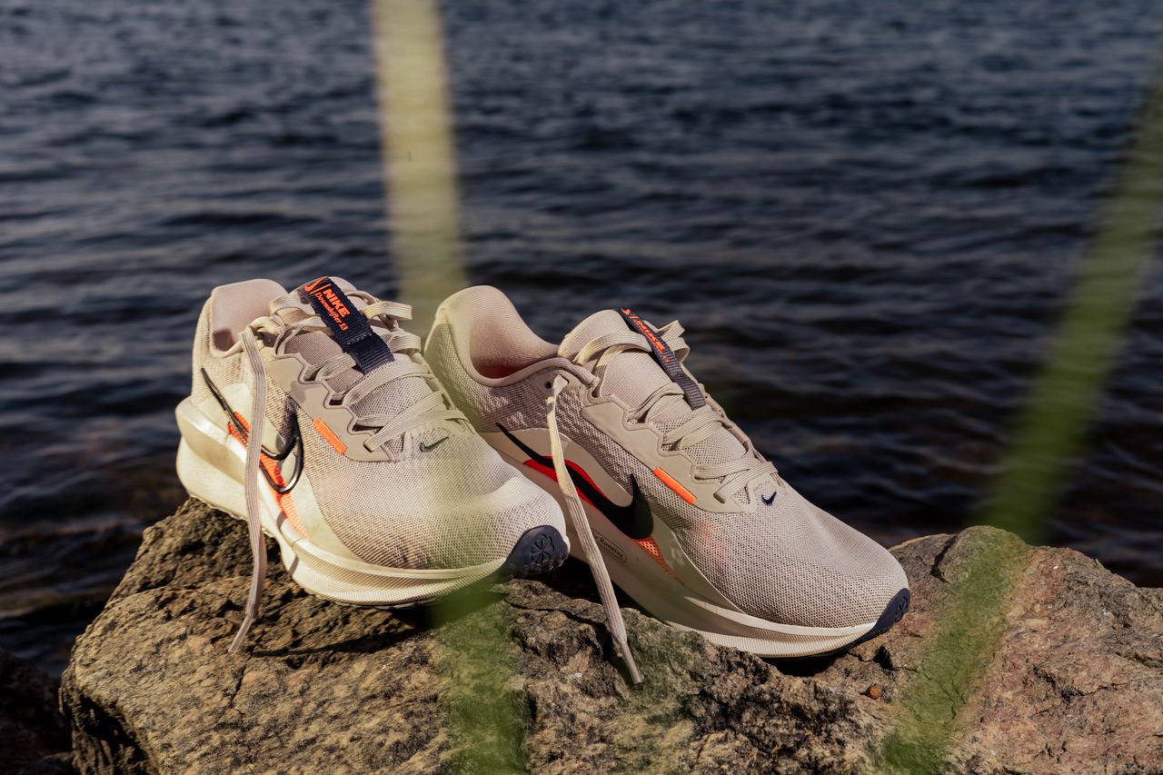 A pair of light gray running shoes resting on rocks by the water, under daylight.
